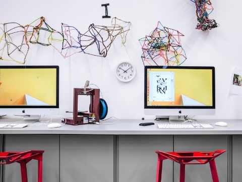 Computers sit on a wall-mounted desk, with art projects strewn above. 