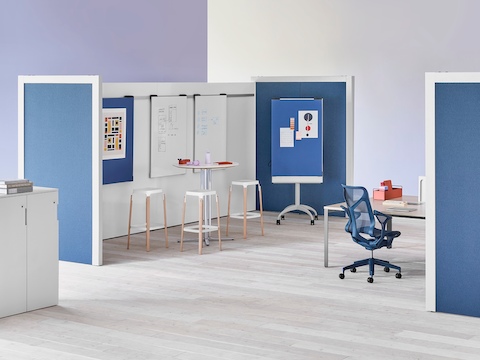 Two Overlay room dividers placed across each other with tables and chairs in between with markerboards in the interior and dark blue fabric on the exterior.