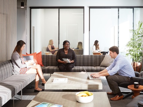 Duas mulheres e um homem trabalhando juntos em um sofá listrado da Tuxedo e em uma lounge chair da Eames na Tavistock Development Company.