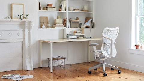 An all-white office with a white Mirra 2 Chair, white desk, Eames LTR table and bookshelves full of books and office accessories.