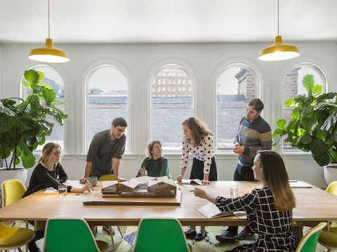 Employés de MASS Design réunis dans une salle de conférence lumineuse équipée d'un grand nombre de sièges Eames Shell jaunes et verts.