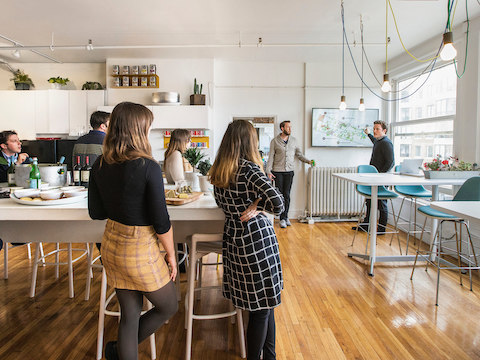 Kantoormedewerkers luisteren naar de presentatie van een collega in een multifunctionele ruimte met vensters.