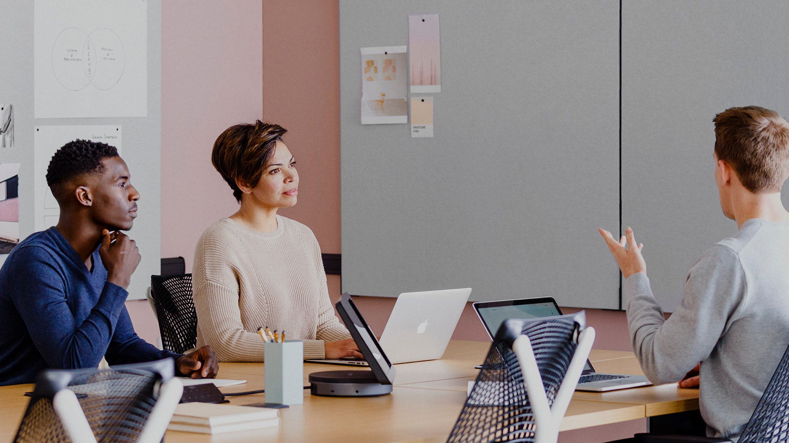 People meeting at seated-height tables with project work pinned on boards attached to the wall.