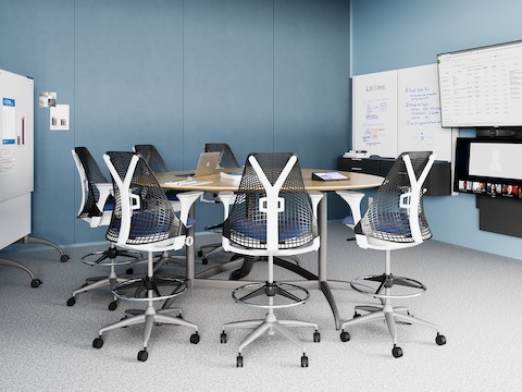 A light blue meeting space with a round table and Sayl Stools, featuring the technology from Logitech.