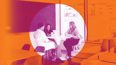 People meeting at a seated-height, round table next to a chalkboard. The image has been retouched to pink and has an orange, transparent graphic overlay with a circle in the middle.