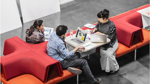 Een man en twee vrouwen werken samen in een opstelling van rode Public Office Landscape stoelen.