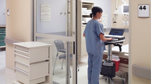 A healthcare professional enters data into a computer, while a Caper Stacking Chair sits in the background. 