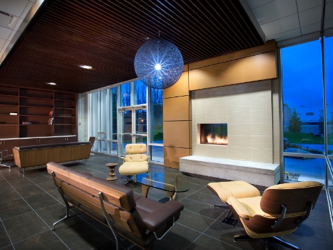 Benches and reclined seating occupy a lounge area centered around a fireplace. Benches and reclined seating occupy a lounge area centered around a fireplace.