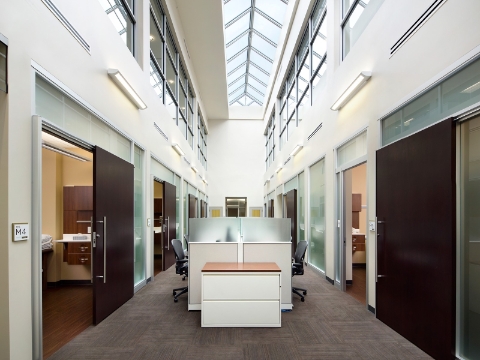 A desk setup sits in the middle of a corridor, flanked by exam rooms. 