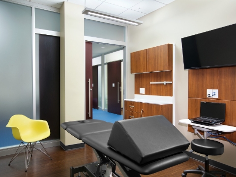 An empty exam room with a yellow Eames molded plastic chair. 