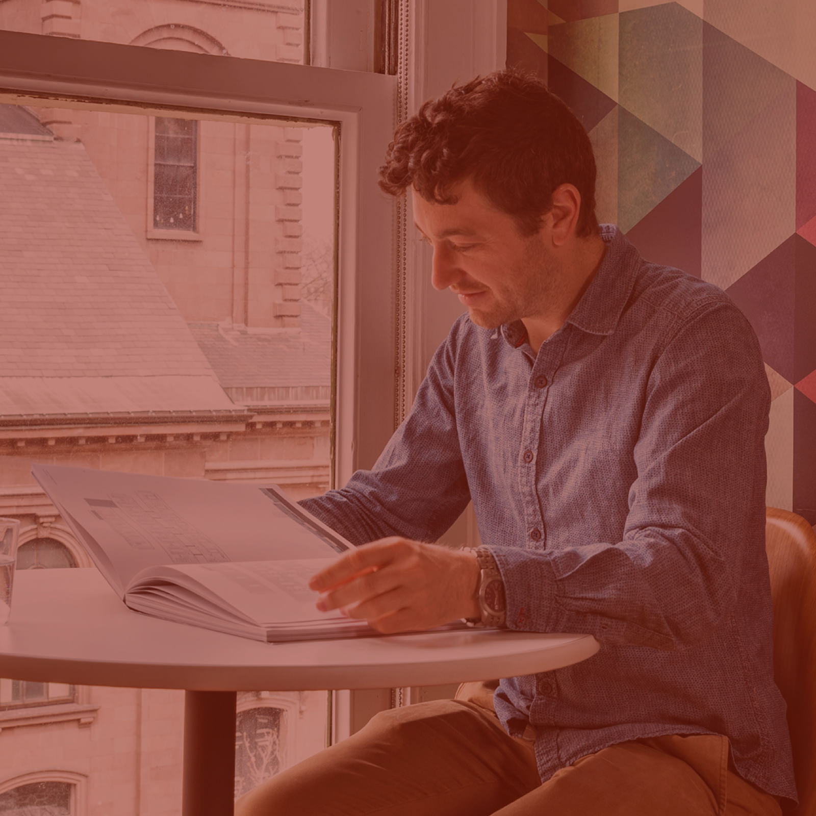 A person sits at a high top desk and reads a book. The surrounding office is bright and airy, and is outfitted with design elements that reflect the company's brand.