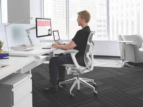 Profile view of a man in a Mirra 2 office chair viewing a monitor attached to an adjustable arm.