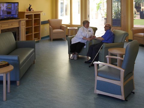 A staff member converses with a resident inside of an assisted living center's lounge. 