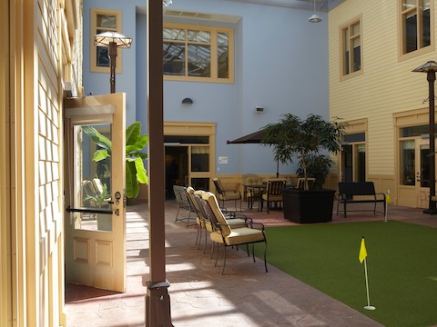 An indoor lounge area with natural light and a putting green surface. 