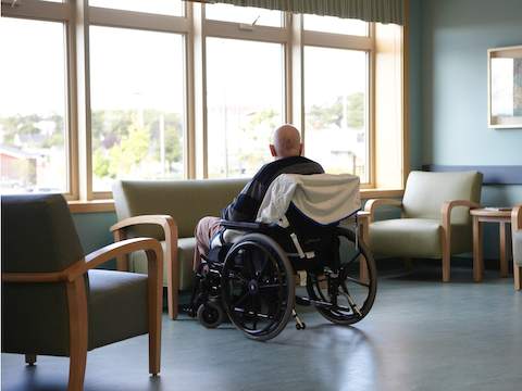 An assisted living resident sits inside a wheelchair while gazing out of a window. 