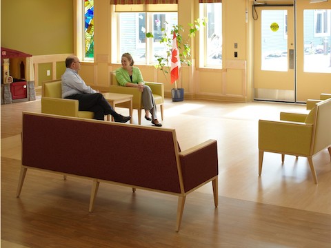 Two people talk while sitting inside of a multi-purpose room amidst various lounge seating.