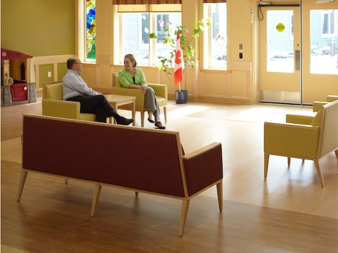 Two people talk while sitting inside of a multi-purpose room amidst various lounge seating. Two people talk while sitting inside of a multi-purpose room amidst various lounge seating.
