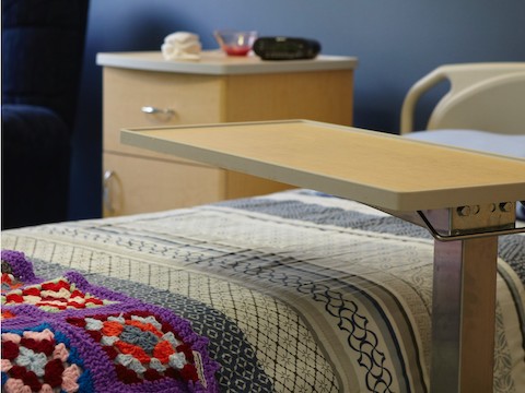 A food tray sits above a made bed inside of a resident room. 