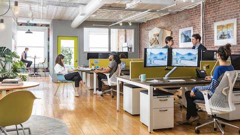 Personas trabajando y colaborando en sus escritorios en un entorno de oficina abierta.