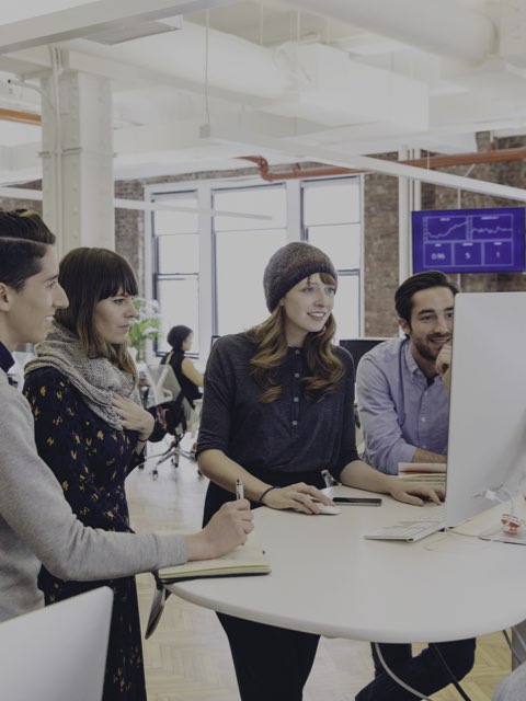 Two women and two men gather round a standing-height table to view a computer monitor.