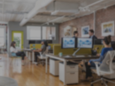 A blurred-back photograph of young people working in an office with vibrantly-colored furniture and art on the walls. A blurred-back photograph of young people working in an office with vibrantly-colored furniture and art on the walls.