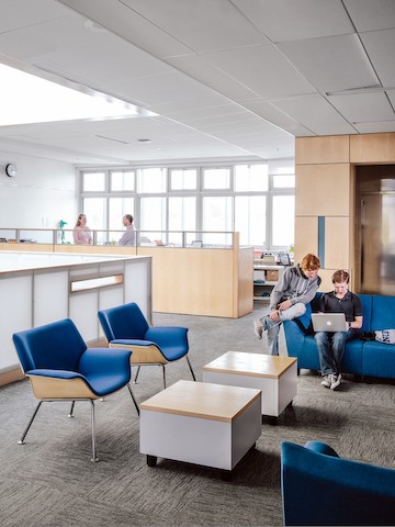 Two college students peer at a laptop computer in a casual seating area featuring blue Swoop Lounge Furniture 