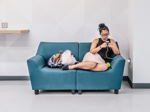 A student checks her smartphone while relaxing with her feet up on a blue loveseat formed from Swoop modular seating elements. 