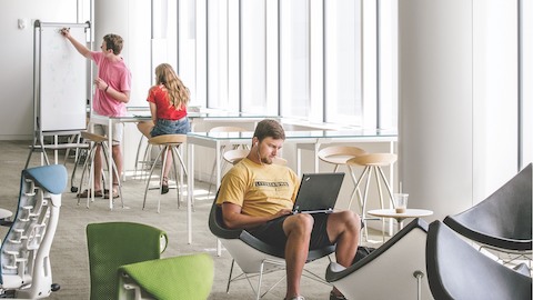 Three college students work in a study area featuring blue and green Embody Chairs.