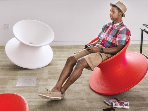 A male college student reclines in a red Magis Spun Chair with a white Magis Spun Chair nearby. A male college student reclines in a red Magis Spun Chair with a white Magis Spun Chair nearby.