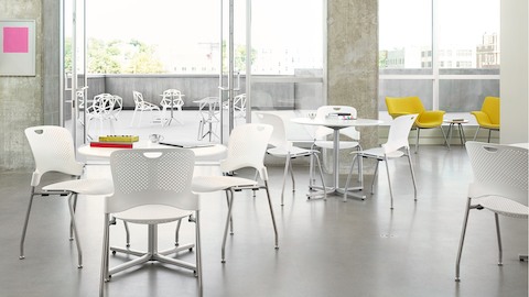 A student gathering space with floor-to-ceiling windows, white Caper Stacking Chairs, and yellow Swoop Lounge Chairs.