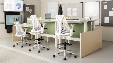 Sayl chairs and stools with white frames and black seats, paired with height-adjustable tables in a healthcare benching application.