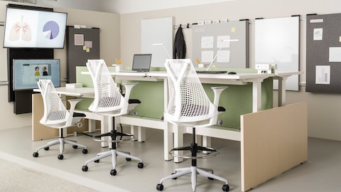 Sayl chairs and stools with white frames and black seats, paired with height-adjustable tables in a healthcare benching application.