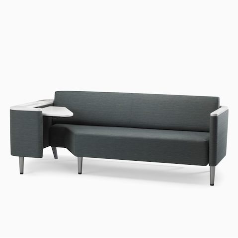 A Palisade Flop Sofa in dark gray textile with white solid surface arm caps and white adjustable table with Durawrap top.
