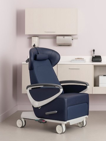 An exam room with an Ava Recliner in a dark blue upholstery and white base and arms with urethane arm caps and Mora System casewok behind it in a light ash finish. An exam room with an Ava Recliner in a dark blue upholstery and white base and arms with urethane arm caps and Mora System casewok behind it in a light ash finish.