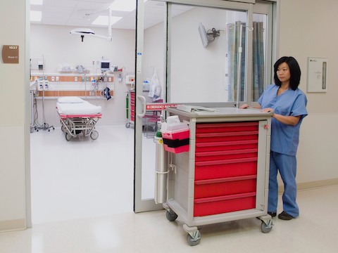 A nurse pushes a mobile Procedure/Supply Cart with seven interchangeable drawers.