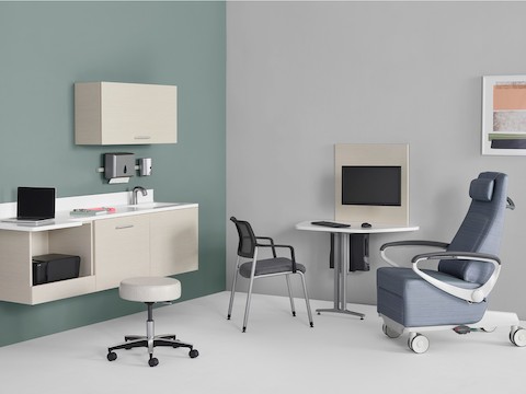 An exam room setting with Mora System casework on the wall in a light wood finish and a Mora peninsula on the side wall located between an Ava patient recliner and a Verus Side Chair.