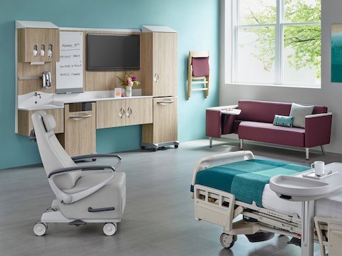 A patient room with a bed, recliner, guest sofa, and Compass System modular storage.