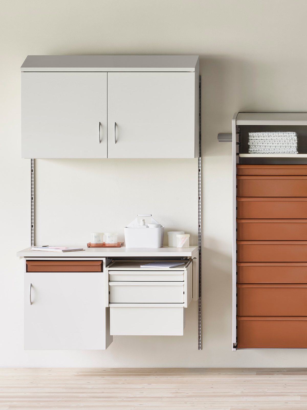 Medical clean utility supply room in soft white Co/Struc System, procedure and supply lockers with terra cotta drawers, and a stainless steel wire shelving unit.