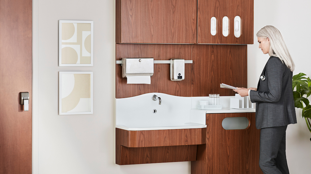 Patient room Compass caregiver work wall in a medium walnut finish with a physician standing and reviewing notes.