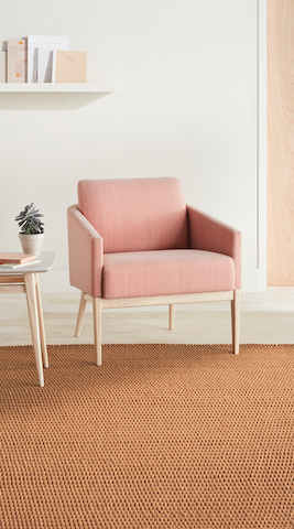 A waiting room with a light pink Palisade Lounge Chair with an ash wood base and a side table with a white solid surface top and an ash wood base.