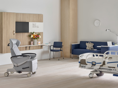 Patient room footwall of Compass System in a medium wood finish, a gray Ava patient recliner chair, a blue Verus Side Chair, a blue Palisade Flop Sofa, and a hospital bed.