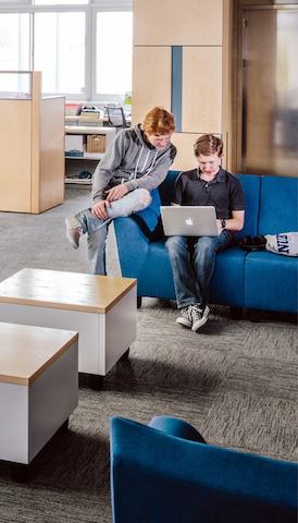 Two college students peer at a laptop computer in a casual seating area featuring blue Swoop Lounge Furniture.