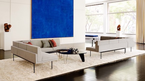 Duas secções Tuxedo em cor marfim proporcionam uma sala de estar num espaço luminoso com uma grande arte azul na parede.