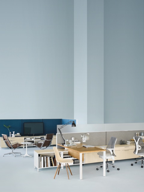 Two brown leather Eames Aluminum Group Chairs and a Nelson Pedestal Table anchor a casual sitting area in an open workplace.