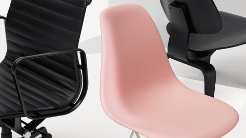 Partial views of a black Eames Aluminum Group Chair, pink Eames Molded Plastic Chair, and black Eames Molded Plywood Chair.