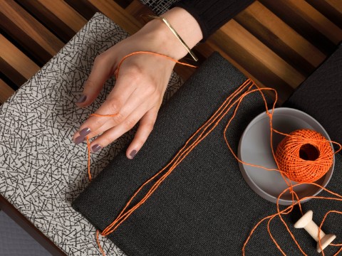 A vignette that includes a woman's hand, orange twine, two material samples, and a Nelson Platform Bench.