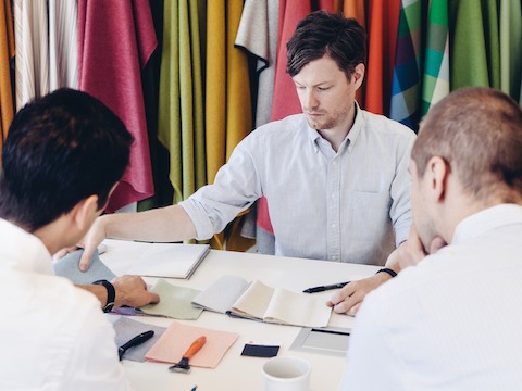 Three seated men review fabric samples.