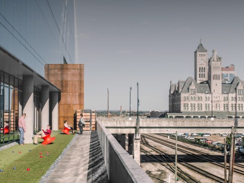 Four people interact outside a modern building, on a grassy area overlooking railroad tracks. Four people interact outside a modern building, on a grassy area overlooking railroad tracks.