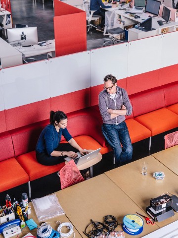 男性と女性が非公式のコーブセッティングで会う。彼らは赤いPublic Office Landscape setteeに座っています。