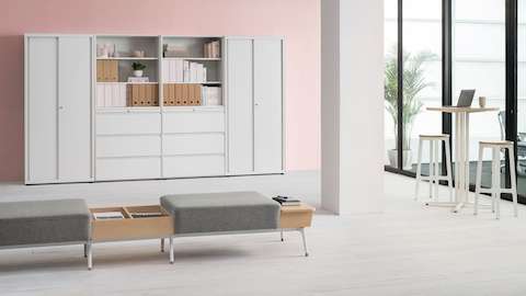 A CK Storage high cabinet wall in 4 pieces sits against a pink wall. A Sabha bench seat is featured along with a high Anywhere Table and Steelwood Stools.